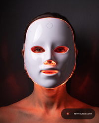 Revival Aura LED face mask worn straight-on, warm ember-red light glowing through the eye, nose, and mouth cutouts